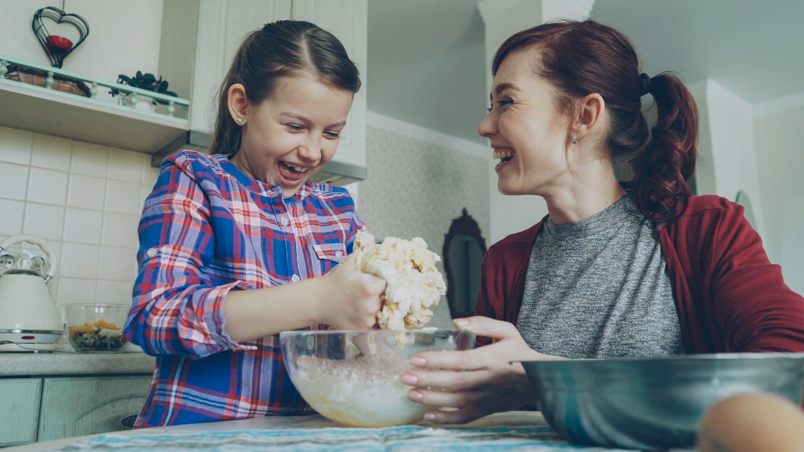Una madre y su hija se ríen mientras preparan masa juntas en la cocina