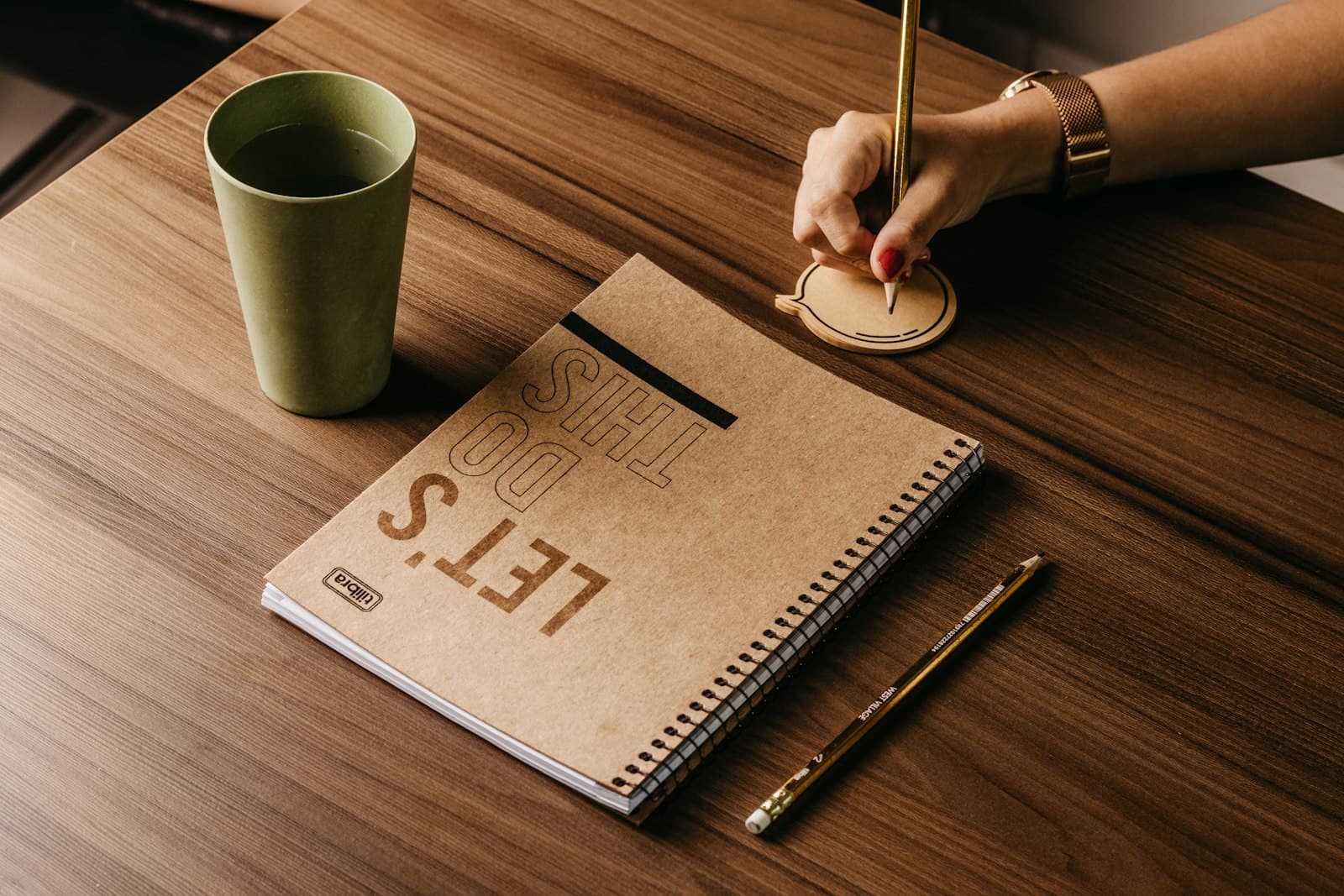 Una persona escribe en un cuaderno junto a una taza de café